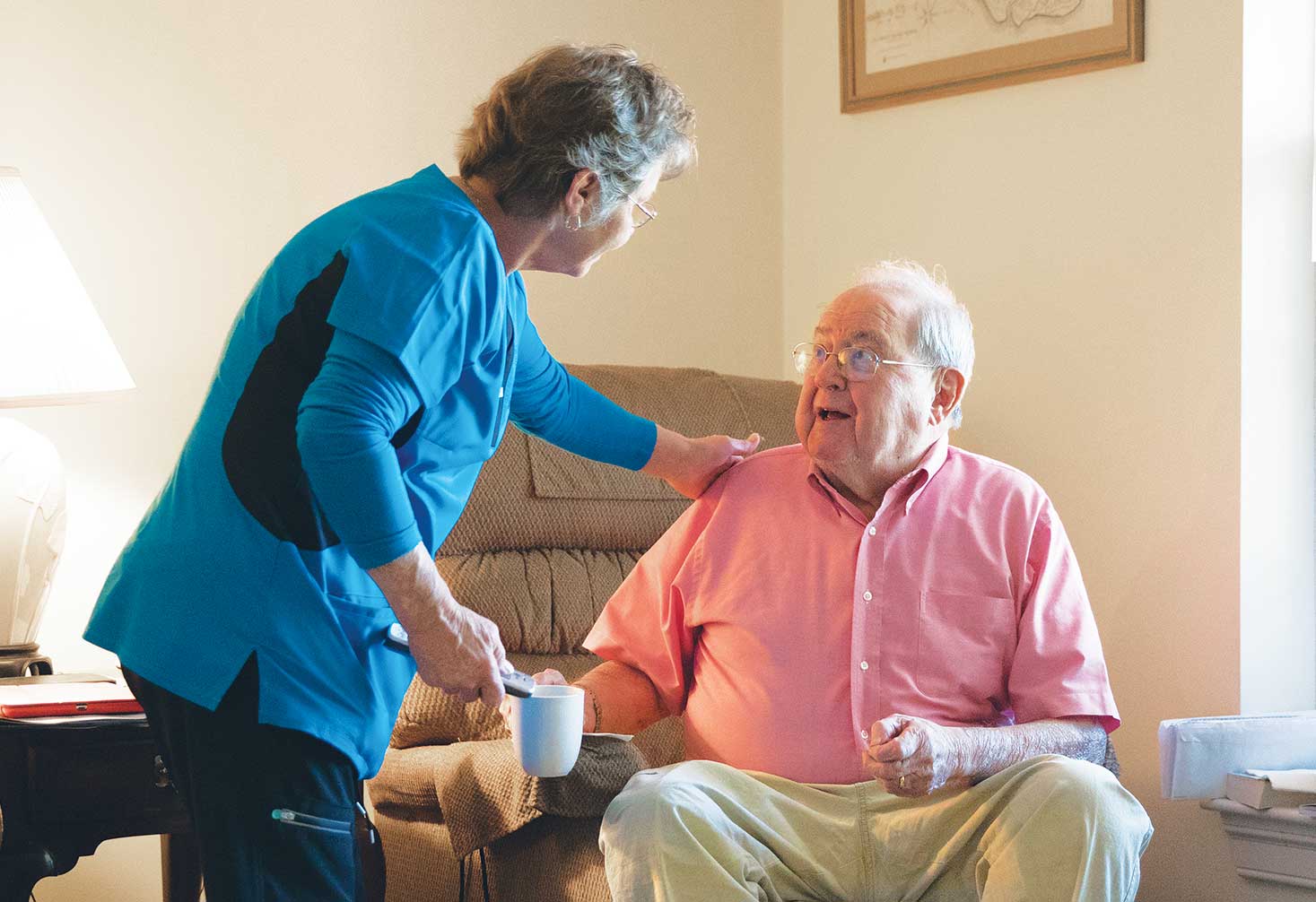 FirstLight Caregiver of the Year, Debbie, leans over to speak to a seated client